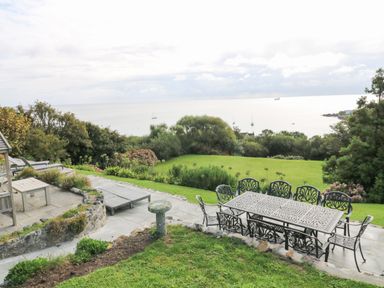 An outdoor patio area with metal table and chairs overlooking a lawn garden and sea at Penmarth House in Coverack