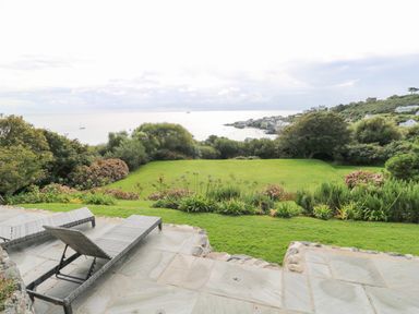 A garden with lawn chairs overlooking a green lawn and coastal houses at Penmarth House in Coverack