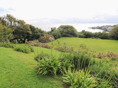 A garden with green grass and plants overlooking the sea with a coastal village at Penmarth House in Coverack