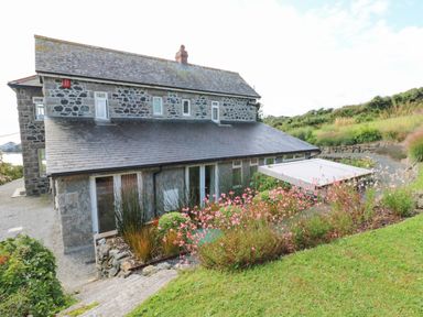 A stone house with multiple windows and a slate roof surrounded by a garden with pink flowers at Penmarth House in Coverack