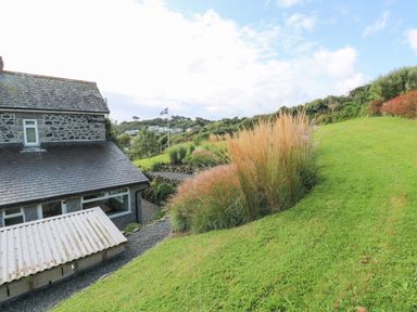 Exterior of a stone house with a slate roof and green garden with tall grasses at Penmarth House in Coverack