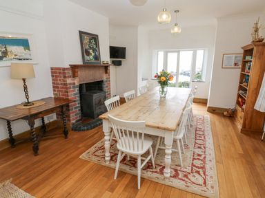 A dining room with a wooden table and white chairs a fireplace and a bookshelf at Penmarth House in Coverack