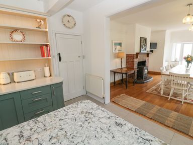A kitchen with green cabinets and marble countertop leading to a dining room with wooden table chairs and a fireplace at Penmarth House in Coverack
