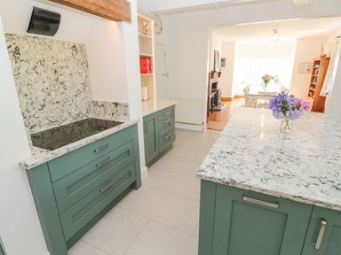 A kitchen with green cabinets and marble countertops and an adjoining dining area at Penmarth House in Coverack
