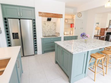 A kitchen with green cabinets a marble island countertop wooden stools a double refrigerator and a sink at Penmarth House in Coverack