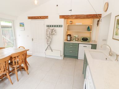 A kitchen with wooden dining table and chairs ironing board and appliances at Penmarth House in Coverack