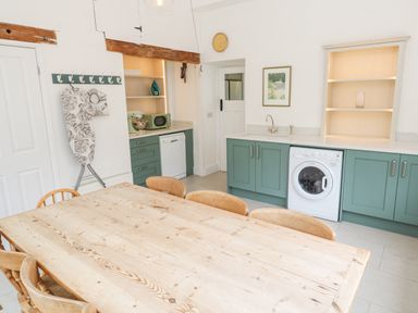 A kitchen with green cabinets a washing machine dishwasher and a wooden dining table with chairs at Penmarth House in Coverack