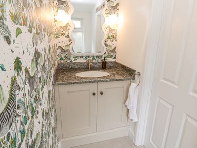A bathroom vanity with a granite countertop a sink a mirror and decorative wallpaper at Penmarth House in Coverack