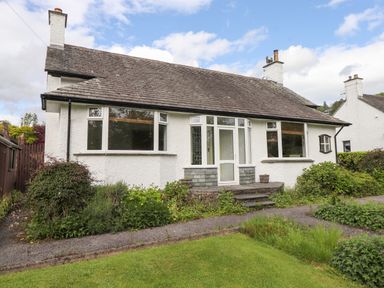 A front view of a single-story house with white exterior walls a tiled roof plants and shrubs in the garden at Halewood in Bowness-On-Windermere