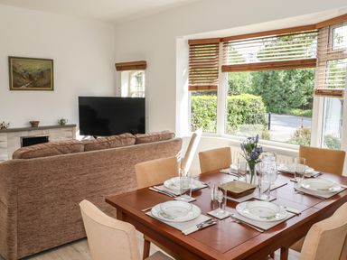 A dining table set with plates glasses and cutlery next to a sofa and a television in a living room at Halewood in Bowness-On-Windermere