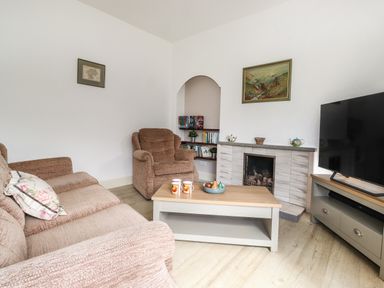 A living room with a sofa, armchair, coffee table, fireplace, TV, and bookshelf at Halewood in Bowness-On-Windermere
