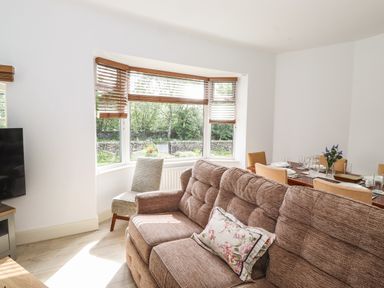 A living room with a brown sofa a single chair and a dining table set with plates and glasses at Halewood in Bowness-On-Windermere