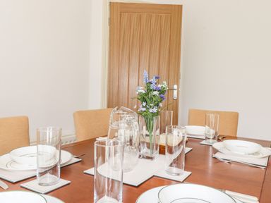 A dining table set with plates bowls glasses a water jug and a vase with flowers at Halewood in Bowness-On-Windermere