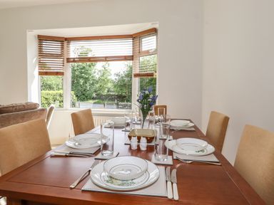 A dining room with a wooden table set with plates glasses cutlery and a vase with flowers at Halewood in Bowness-On-Windermere