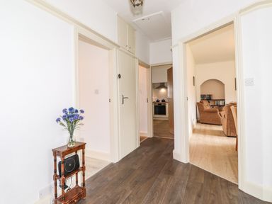 A hallway with wooden floor and white walls with a small wooden shelf holding a vase of flowers at Halewood in Bowness-On-Windermere