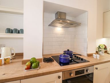 A kitchen with a stovetop and two blue pots on it a kettle cups and a tray of fruit on the counter at Halewood in Bowness-On-Windermere