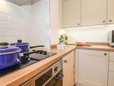 A kitchen counter with two blue pots on a stove bread on a cutting board and a microwave at Halewood in Bowness-On-Windermere