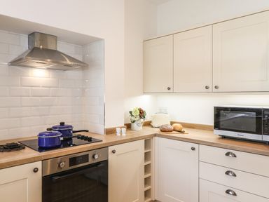 A kitchen with cream cabinets a stovetop with two blue pots a toaster bread on a cutting board and a microwave at Halewood in Bowness-On-Windermere