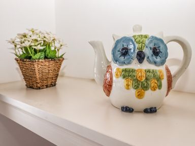 A ceramic owl-shaped teapot and a wicker basket with white flowers on a shelf at Halewood in Bowness-On-Windermere