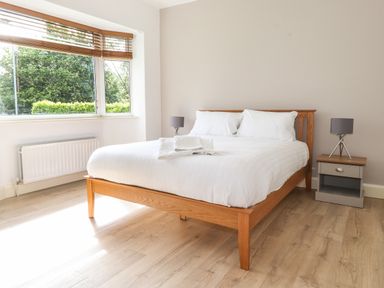 A bedroom with a wooden bed white bedding bedside tables with lamps and a large window at Halewood in Bowness-On-Windermere