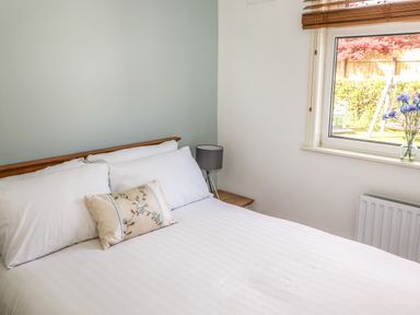 A bedroom with a bed white pillows a side table lamp and a window with flowers on the sill at Halewood in Bowness-On-Windermere
