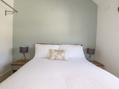 A bedroom with a bed white sheets pillows and two bedside tables with lamps at Halewood in Bowness-On-Windermere
