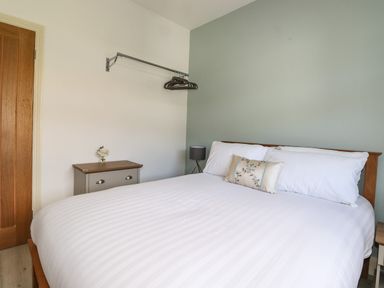 A bedroom with a bed with white linens and pillows bedside tables a lamp a small chest of drawers a wooden door and a wall-mounted clothes rail with hangers at Halewood in Bowness-On-Windermere