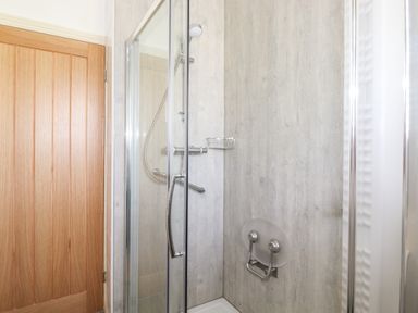 A shower enclosure with glass doors a wall-mounted showerhead and a wooden door at Halewood in Bowness-On-Windermere