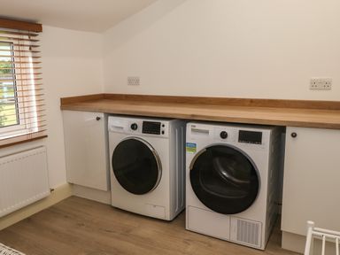 A laundry room with a washing machine and dryer under a wooden counter at Halewood in Bowness-On-Windermere