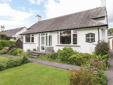 A white house with a tiled roof and a garden with shrubs and flowers at Halewood in Bowness-On-Windermere