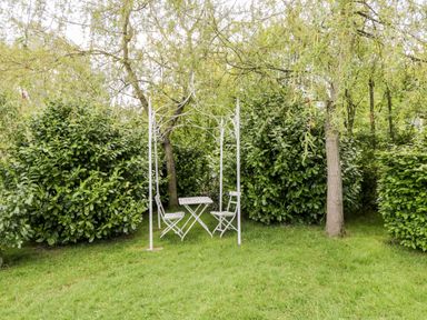 A white metal table and two chairs under a metal arch surrounded by trees and bushes at The River House Avon Valley Stonehenge with fishing in Salisbury