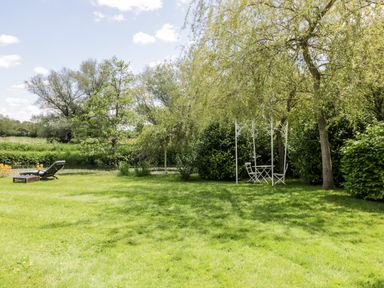 A garden with a lawn chair and a white table with two chairs under a tree at The River House Avon Valley Stonehenge with fishing Salisbury
