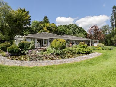 A house with a garden pond and trimmed bushes in front at The River House Avon Valley Stonehenge with fishing Salisbury
