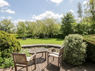 A garden with wooden chairs and table near a pond with lily pads and trees at The River House Avon Valley Stonehenge with fishing in Salisbury