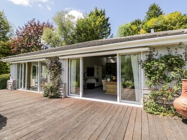A wooden deck outside a house with sliding glass doors and climbing plants at The River House Avon Valley Stonehenge with fishing Salisbury