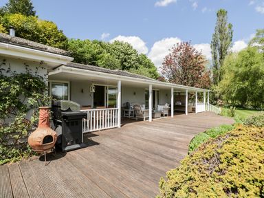 A wooden deck with outdoor seating and a barbecue grill outside a house surrounded by trees at The River House Avon Valley Stonehenge with fishing Salisbury