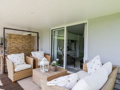 A covered patio with wicker furniture and cushions outside sliding glass doors at The River House Avon Valley Stonehenge with fishing Salisbury