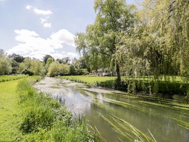 A river flowing through grass and trees with a house in the background at The River House Avon Valley Stonehenge with fishing Salisbury