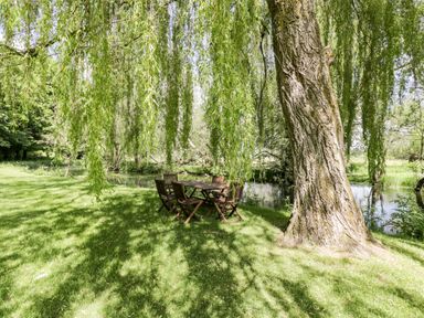 Wooden table and chairs under willow tree near river at The River House Avon Valley Stonehenge with fishing Salisbury
