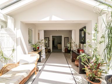 A sunlit hallway with plants a wicker bench and tables at The River House Avon Valley Stonehenge with fishing Salisbury
