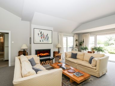 A living room with two beige sofas a wooden coffee table a fireplace and large windows at The River House Avon Valley Stonehenge with fishing Salisbury