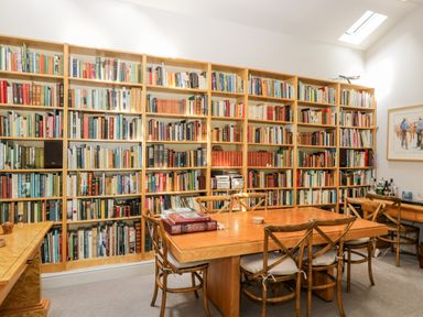 A room with bookshelves filled with books a wooden table and chairs and a painting on the wall at The River House Avon Valley Stonehenge with fishing Salisbury