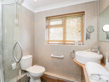 A bathroom with a toilet a glass shower a sink with a wooden counter and a window with blinds at The River House Avon Valley Stonehenge with fishing Salisbury