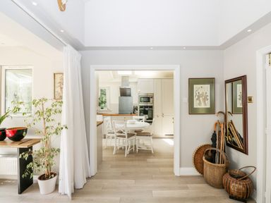 A hallway with a round dining table and chairs visible in the kitchen and an umbrella stand and wicker baskets at The River House Avon Valley Stonehenge with fishing Salisbury