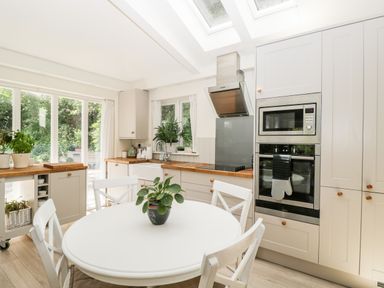 A kitchen with a round table and chairs a microwave and oven and plants on a windowsill at The River House Avon Valley Stonehenge with fishing Salisbury
