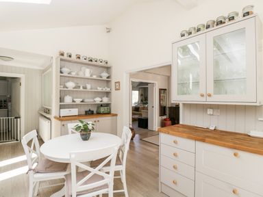 A kitchen with a round table and four chairs a shelf with crockery cupboards and a countertop at The River House Avon Valley Stonehenge with fishing Salisbury