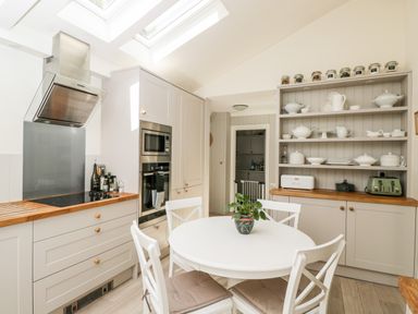 A kitchen with a round white dining table and four chairs a stove with an oven a microwave a cupboard with dishes spices and kitchen appliances at The River House Avon Valley Stonehenge with fishing Salisbury