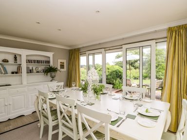 A dining room with a white table set for eight and a white cabinet by the wall with books at The River House Avon Valley Stonehenge with fishing Salisbury