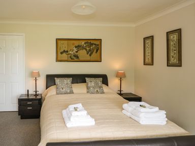 A bedroom with a bed covered in a beige quilt and two stacks of white towels on it with two bedside tables and lamps at The River House. Avon Valley. Stonehenge (with fishing) Salisbury