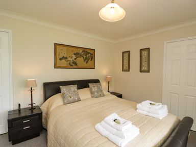 A bedroom with a bed covered in a beige quilt and two nightstands with lamps at The River House Avon Valley Stonehenge with fishing Salisbury